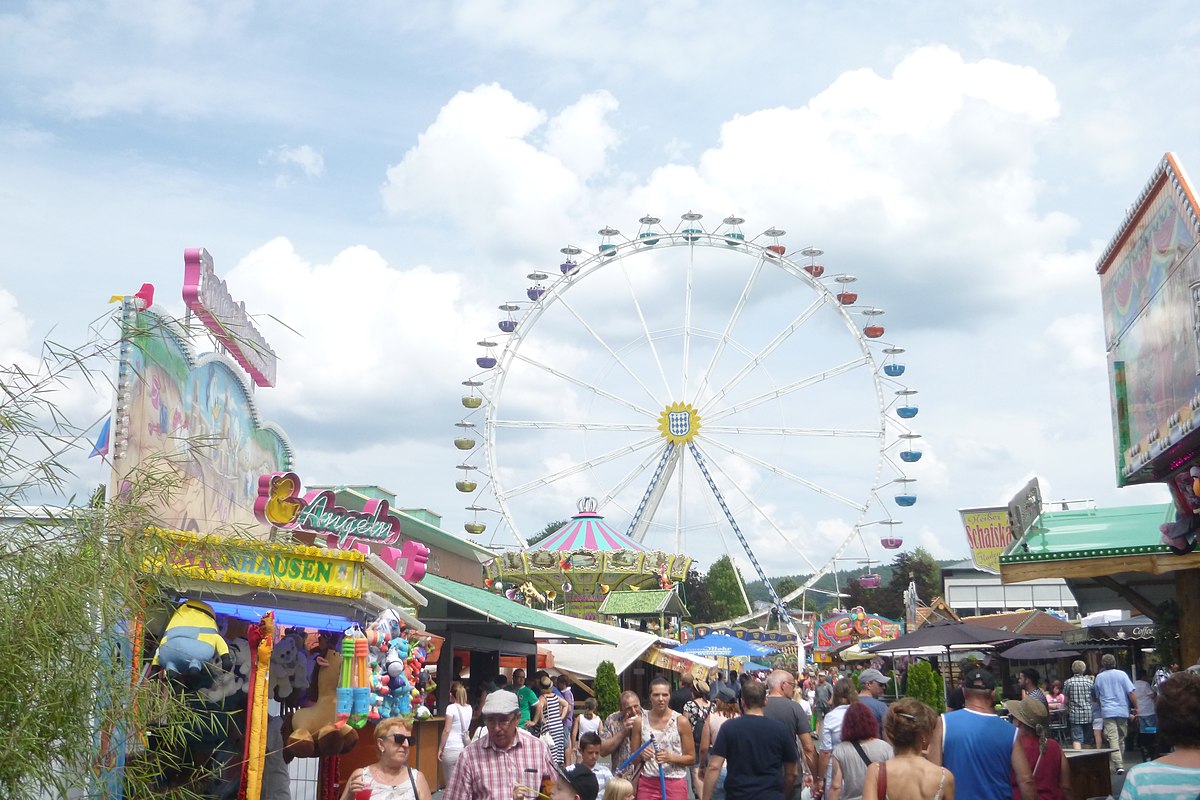 A picture of the ferris wheel towering over a crowd of people who wander between booths of the Erbacher Wiesenmarkt festival